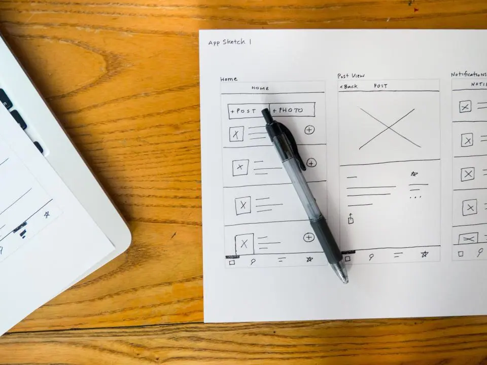 Website wireframe sketches on paper beside a laptop
